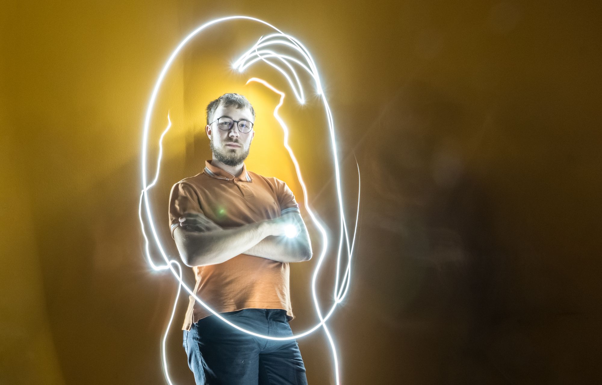 Header Image showing Matthias Mair (male, 175cm, glasses, bearded) leaning on wall (orange), holding a flashlight and being surrounded by light-paintings